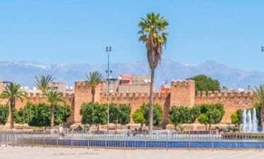 Palmeras y murallas de Marruecos en un parque con montañas al fondo.