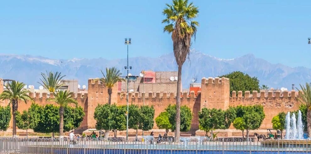 Palmeras y murallas de Marruecos en un parque con montañas al fondo.