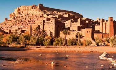 Ancient Moroccan kasbah overlooking the river, desert landscape, and palm trees, ideal for Marruecos travel adventures.